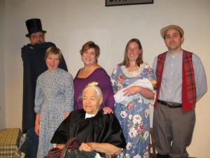 Molly Ferris (seated) along with (standing from left to right) Tom Field, Balley Matteson, Aprille Blanchard, Anna Kendall and Scott Stearns present “Foiled By An Innocent Maid” at BRAM’s ninth annual Christmas celebration.