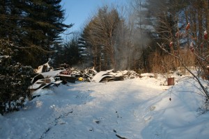 The Sunday morning fire that destroyed a Trebo Road home still smolders on Monday morning. A red tractor can be seen parked on the left. CLICK photo to enlarge. Photos by Shawn Cunningham