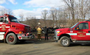 Chester firefighters and state fire inspector confer on Sunday morning with burnt remains of the house in the background.