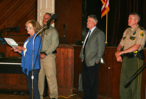 A friend of arson victims reads a letter to the audience explaining their concerns over policing. Behind her, Otis, Flynn and