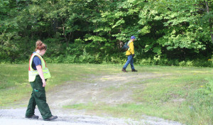 Three firefighters search along Rte 121. The third is deeper into the woods.