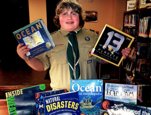 Liam Mallan, 13, standing withbooks that were added to the Rockingham Library's youth collection as a result of his project.